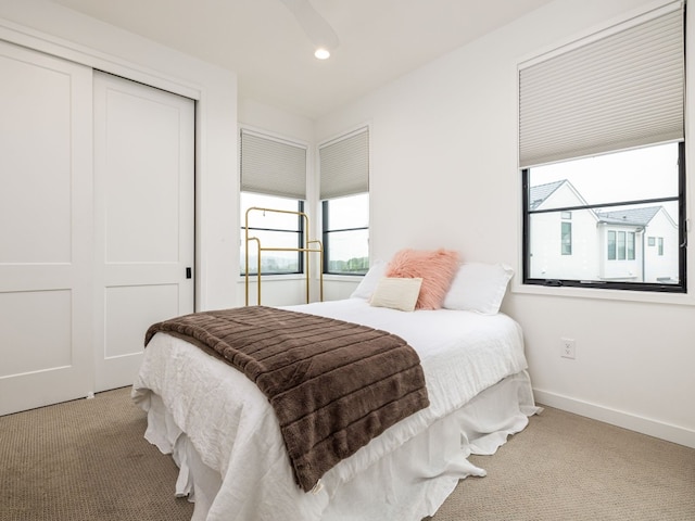 bedroom featuring baseboards, multiple windows, a closet, and light colored carpet