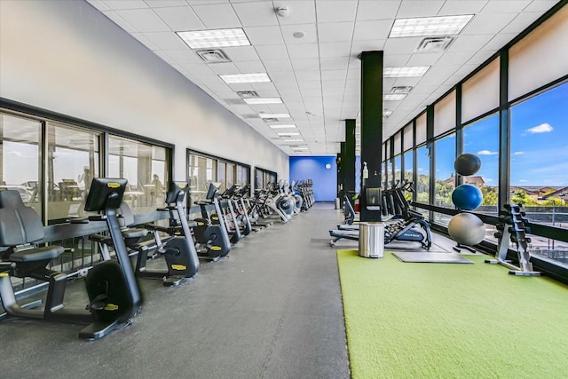 exercise room with a paneled ceiling, floor to ceiling windows, visible vents, and a high ceiling