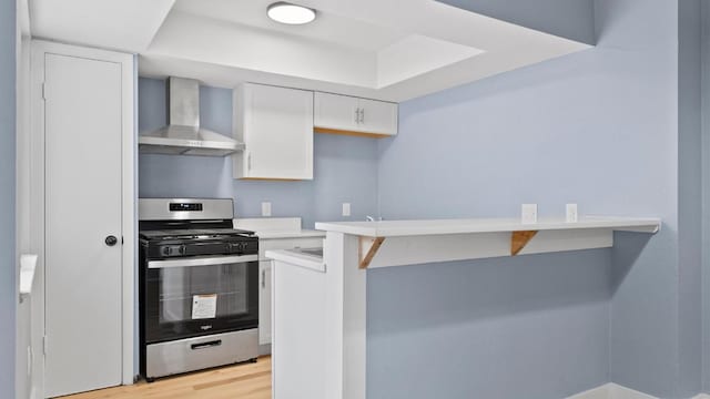 1112 Village Green Dr, Austin, TX 78753 - kitchen with stainless steel gas stove, wall chimney range hood, white cabinets, light wood-type flooring, and light countertops