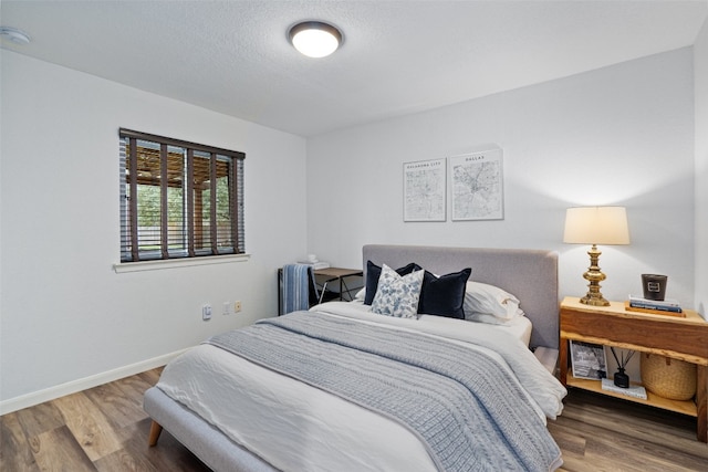 bedroom with a textured ceiling, wood finished floors, and baseboards