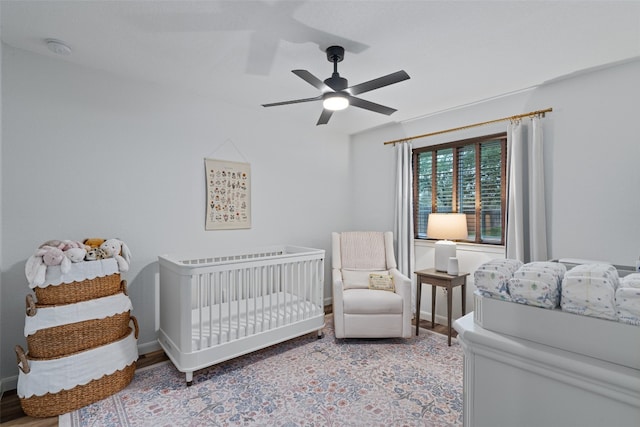 bedroom featuring a ceiling fan, a crib, and wood finished floors