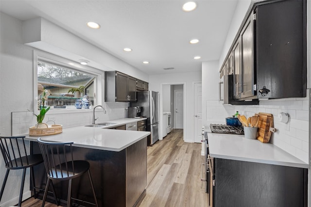 kitchen with appliances with stainless steel finishes, a breakfast bar, a peninsula, light countertops, and a sink