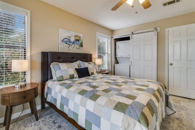 bedroom with stone tile flooring, visible vents, a barn door, stacked washer / dryer, and ceiling fan