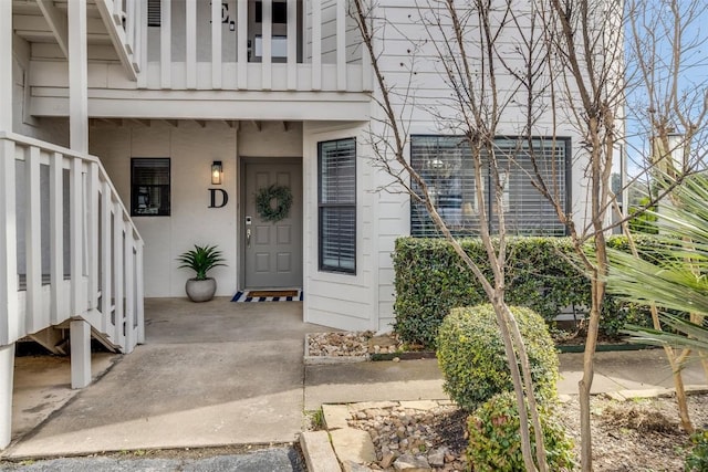 view of exterior entry featuring board and batten siding, a balcony, and stucco siding