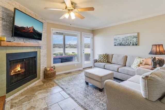 living room with a large fireplace, baseboards, a ceiling fan, stone finish flooring, and crown molding