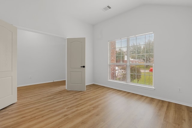 unfurnished room featuring light wood-style floors, visible vents, vaulted ceiling, and baseboards