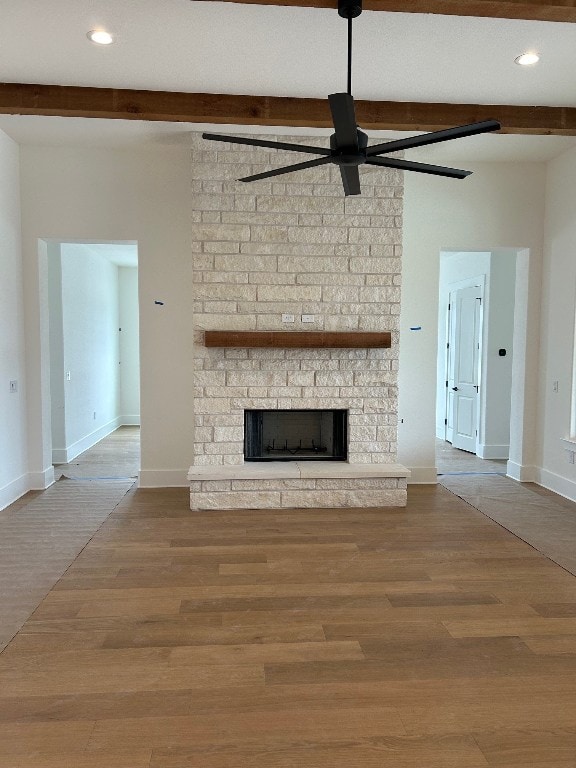 unfurnished living room featuring a fireplace, baseboards, wood finished floors, and beamed ceiling