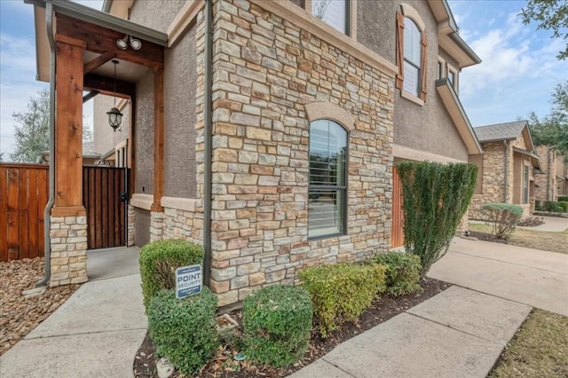 view of side of home with stone siding, fence, and stucco siding