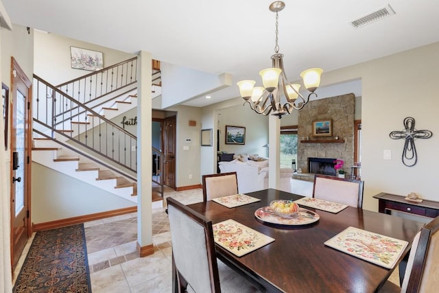 dining area featuring a stone fireplace, visible vents, baseboards, stairs, and an inviting chandelier