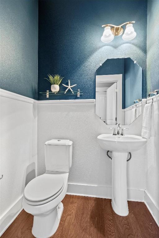 half bathroom featuring a sink, wood finished floors, toilet, and baseboards