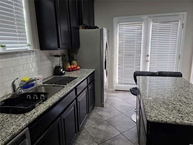 kitchen with dark cabinets, a sink, dishwasher, and light stone countertops