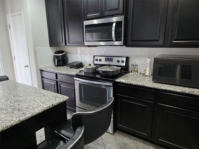 kitchen with light stone countertops, appliances with stainless steel finishes, backsplash, and dark cabinetry