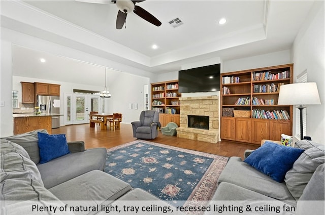 living room featuring a raised ceiling, a fireplace, ceiling fan with notable chandelier, wood finished floors, and visible vents