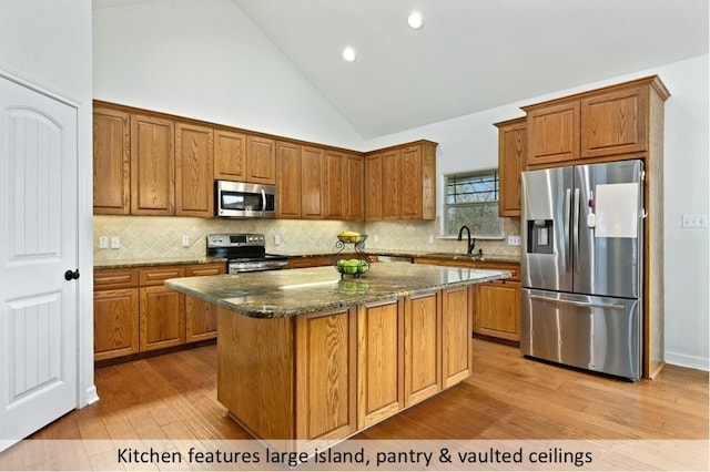 kitchen with appliances with stainless steel finishes, a center island, a sink, light wood-style floors, and dark stone counters