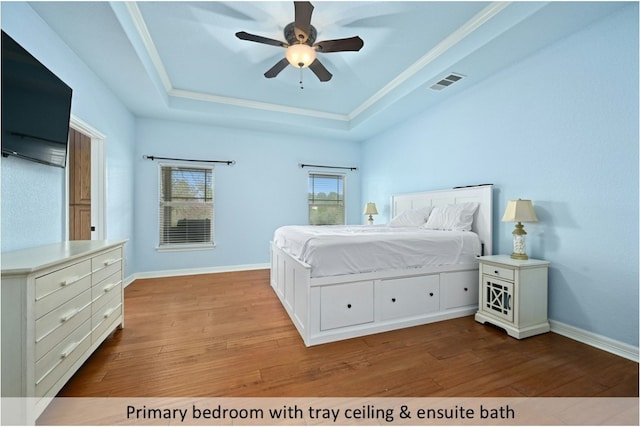 bedroom with ceiling fan, visible vents, wood finished floors, baseboards, and a tray ceiling