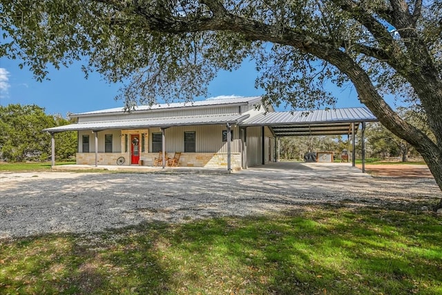 farmhouse-style home with metal roof, covered porch, stone siding, a carport, and gravel driveway