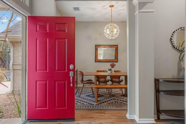 foyer entrance with a chandelier, wood finished floors, visible vents, and baseboards