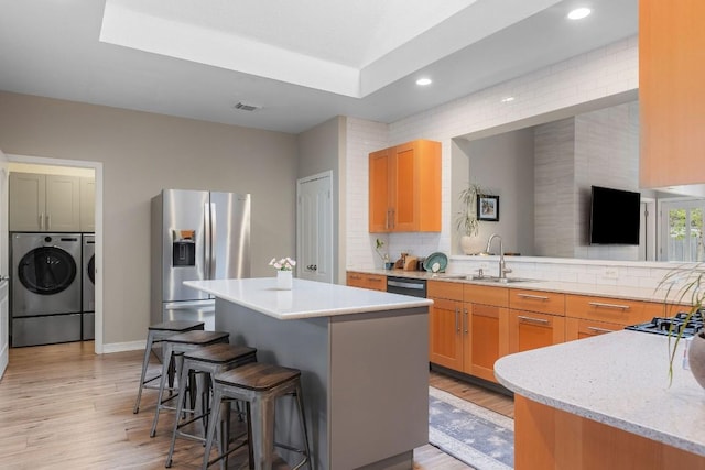 kitchen with stainless steel refrigerator with ice dispenser, washer and clothes dryer, a kitchen island, a sink, and a kitchen breakfast bar