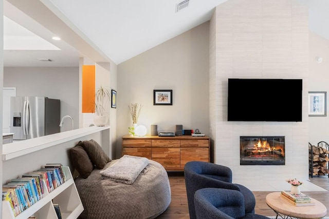 living area featuring visible vents, vaulted ceiling, a tiled fireplace, and wood finished floors