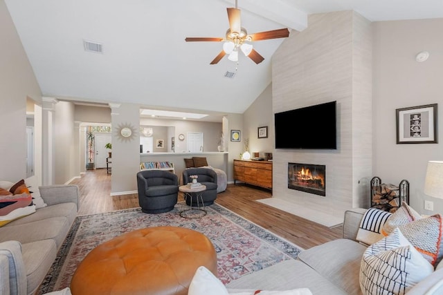 living area with light wood finished floors, decorative columns, visible vents, a tiled fireplace, and beamed ceiling