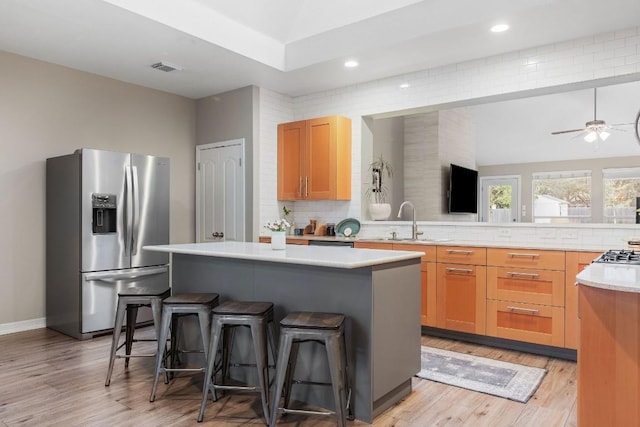 kitchen featuring a breakfast bar, light countertops, appliances with stainless steel finishes, a kitchen island, and a sink