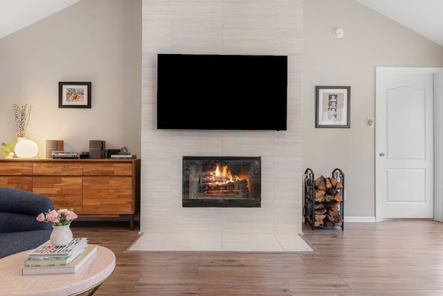 living area featuring lofted ceiling, baseboards, dark wood-style flooring, and a tiled fireplace