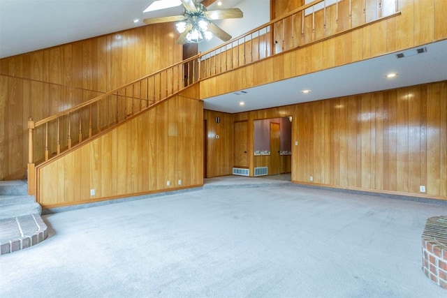 unfurnished living room with wooden walls, visible vents, light colored carpet, a towering ceiling, and stairs