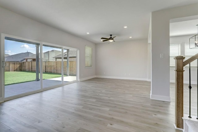 spare room featuring recessed lighting, ceiling fan with notable chandelier, baseboards, stairway, and light wood finished floors