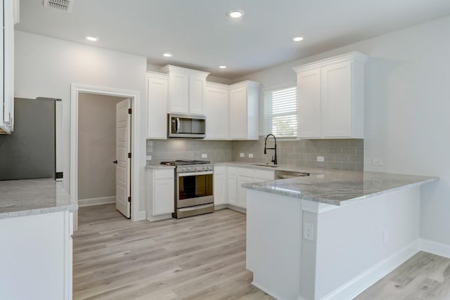 kitchen with appliances with stainless steel finishes, white cabinets, a sink, and a peninsula