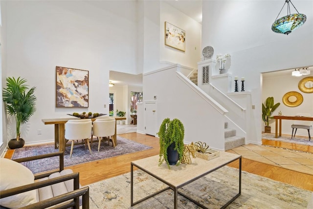 living area with stairway, wood finished floors, a towering ceiling, and baseboards