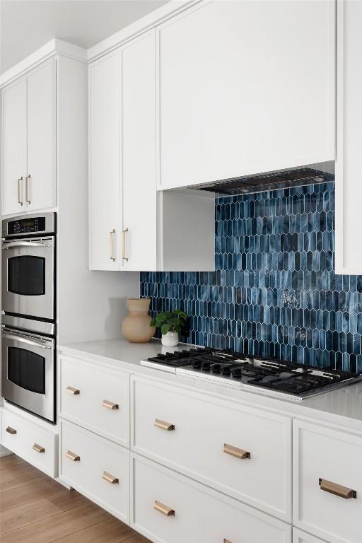 kitchen with light wood-style flooring, stainless steel double oven, white cabinetry, and decorative backsplash