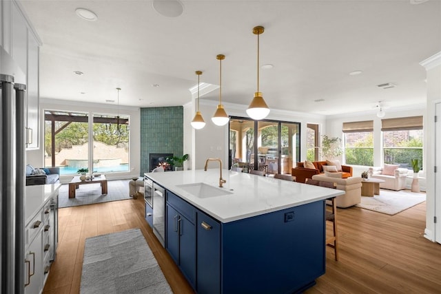 kitchen featuring light countertops, a tiled fireplace, open floor plan, a kitchen island with sink, and a sink