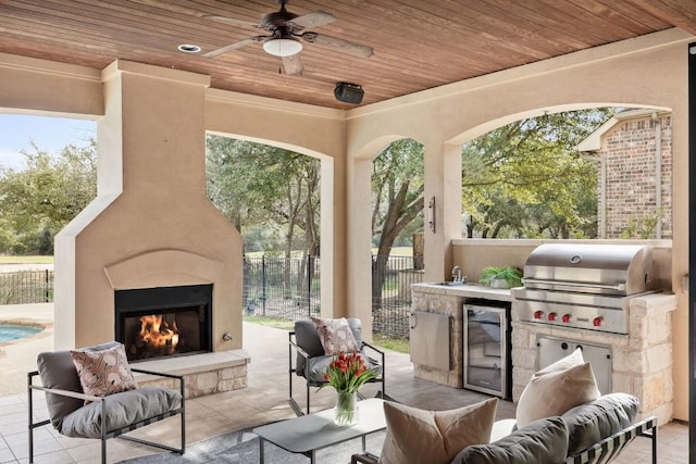 view of patio / terrace with a warm lit fireplace, a ceiling fan, grilling area, fence, and a sink