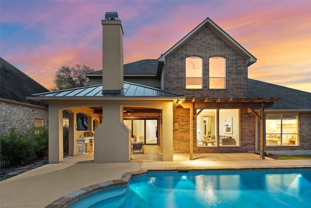 back of property at dusk featuring brick siding, a patio, a chimney, a standing seam roof, and metal roof