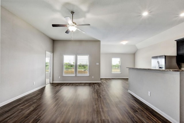 unfurnished living room featuring dark wood-style floors, vaulted ceiling, ceiling fan, and baseboards