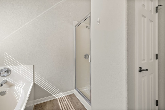 bathroom featuring baseboards, wood finished floors, a bath, and a shower stall