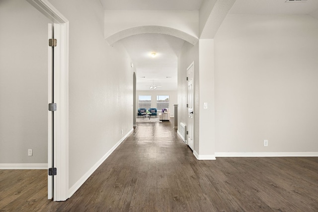 hall with dark wood-style floors, baseboards, visible vents, and arched walkways