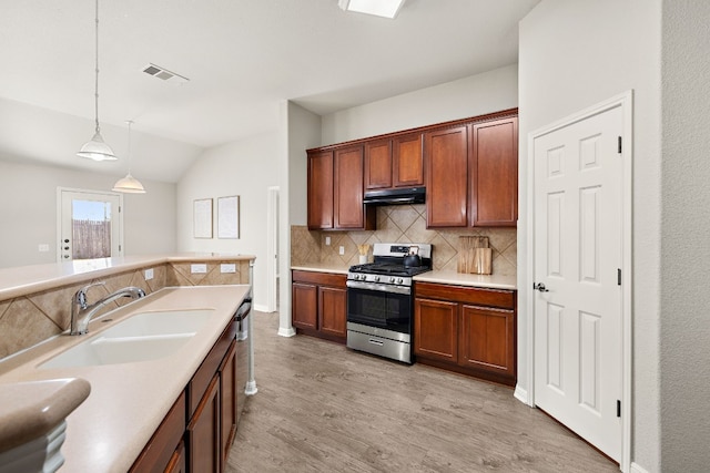 kitchen with decorative light fixtures, light countertops, a sink, under cabinet range hood, and stainless steel gas range oven