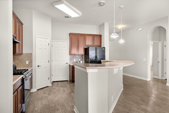 kitchen featuring range with gas cooktop, brown cabinets, decorative light fixtures, black refrigerator with ice dispenser, and light countertops