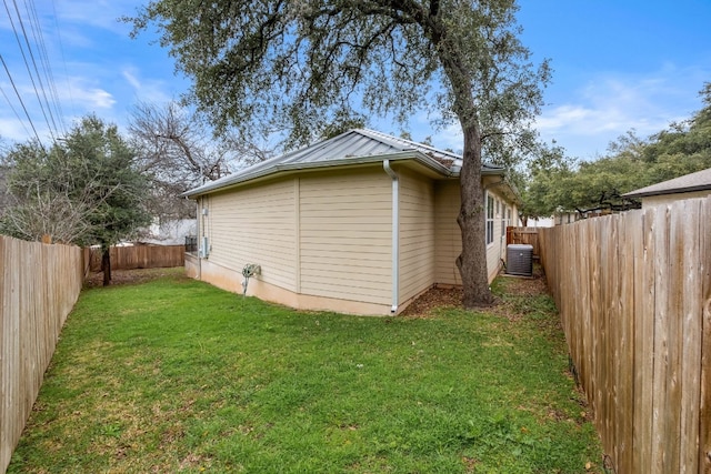 view of side of property featuring a fenced backyard, central AC, metal roof, and a lawn