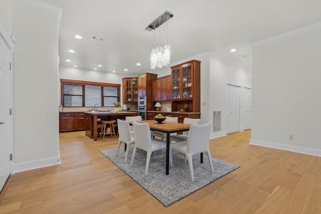 dining space featuring crown molding, light wood-type flooring, visible vents, and baseboards