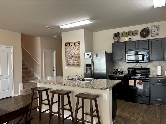 kitchen featuring light stone countertops, black appliances, a breakfast bar area, and a sink
