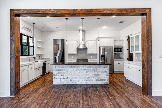 kitchen featuring stainless steel appliances, hanging light fixtures, wall chimney range hood, and white cabinetry