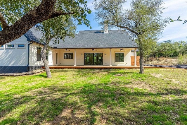 rear view of property featuring a yard, a shingled roof, a chimney, and a ceiling fan