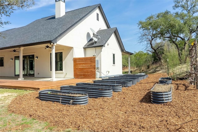 rear view of house featuring a chimney, stucco siding, a shingled roof, ceiling fan, and a wooden deck