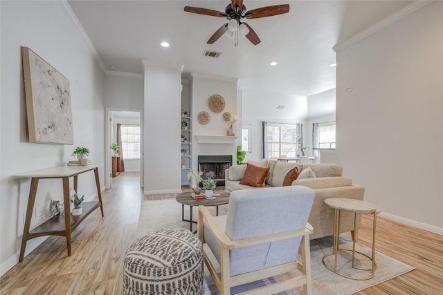 living room featuring light wood-type flooring, plenty of natural light, a fireplace, and crown molding