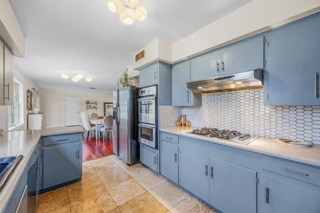 4608 Arapahoe Trl, Austin, TX 78745 - kitchen with under cabinet range hood, blue cabinets, appliances with stainless steel finishes, decorative backsplash, and light countertops