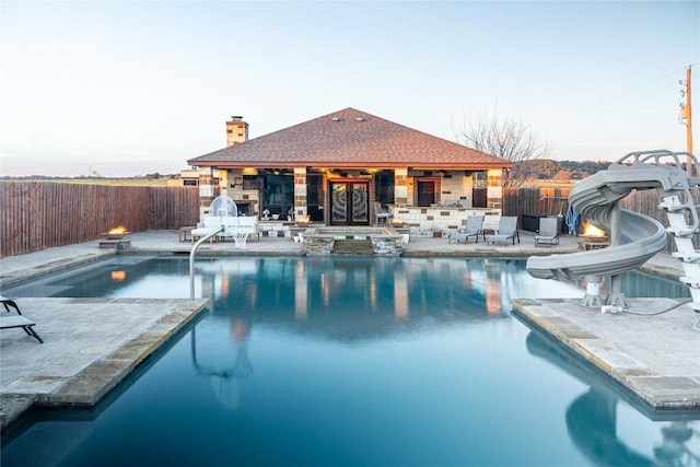 pool at dusk with a patio area, a fenced backyard, a fenced in pool, and a water slide
