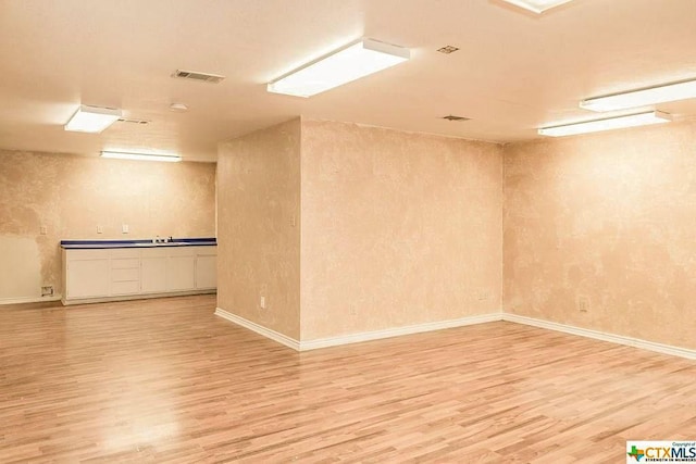 finished basement with baseboards, a sink, visible vents, and light wood-style floors