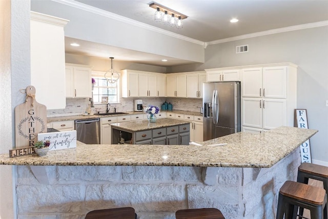 kitchen with a peninsula, a breakfast bar, white cabinets, appliances with stainless steel finishes, and light stone countertops